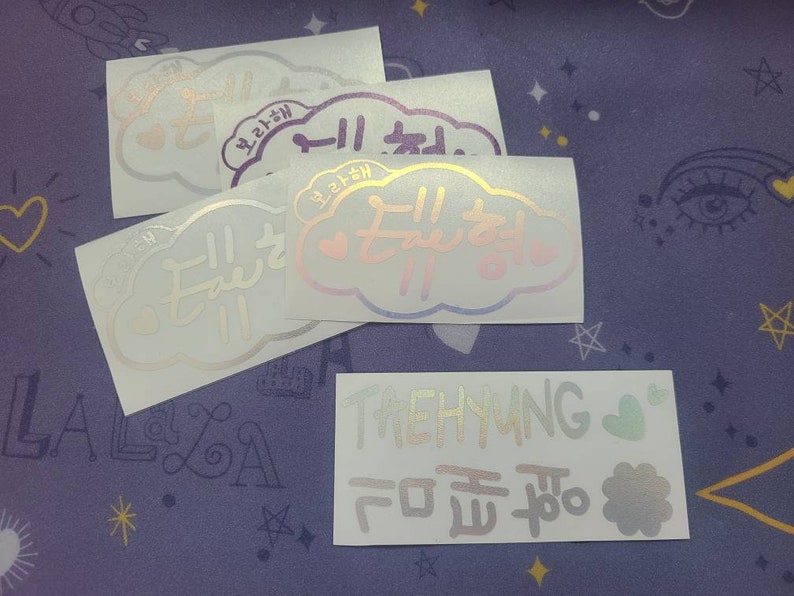 K&ouml;nnte beinhalten: Vier schimmernde Aufkleber mit koreanischem Text. Die Aufkleber haben die Form von Wolken und zeigen ein Herzdesign. Der Text auf den Aufklebern lautet "taehyung" und "ich liebe dich".