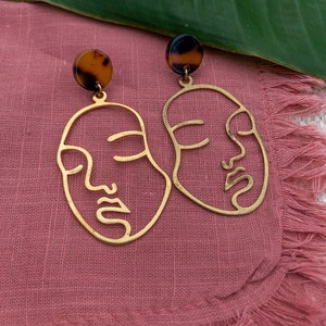 May include: A pair of gold earrings with a face design. The earrings have a tortoiseshell accent at the top.