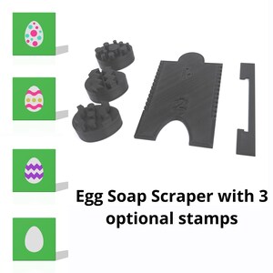May include: A black plastic egg soap scraper with three optional stamps. The stamps are round and have different designs. The scraper has a handle and a notch for holding an egg.