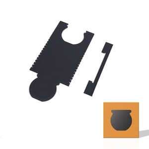 May include: A black cardboard cutout of a cauldron with a handle. The cauldron is on a yellow background. The cutout is designed to be used as a craft project.