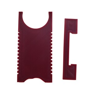 May include: A red plastic tool with a handle and a serrated edge. The tool is designed to scrape and clean surfaces.