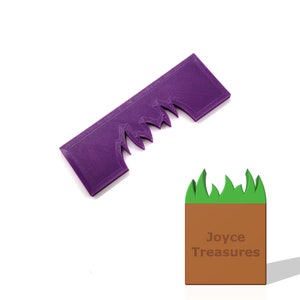 May include: A purple, rectangular object with a jagged edge, resembling a comb or decorative element. The image also includes a brown and green block with the text "Joyce Treasures". The objects are set against a white background.