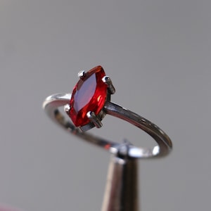 Può includere: Un anello d'argento con una pietra preziosa rossa a forma di marquise.