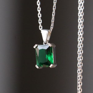 May include: A silver chain necklace with a square emerald green gemstone pendant.
