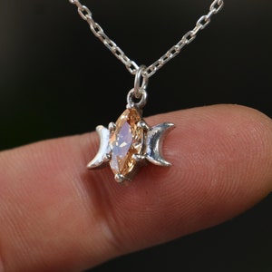 May include: A silver necklace with a pendant featuring a triple moon design and a marquise-shaped topaz gemstone.