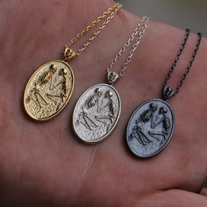 May include: Three silver oval pendants with a skeleton couple design. The pendants are on chains and are in different finishes: gold, silver, and black.