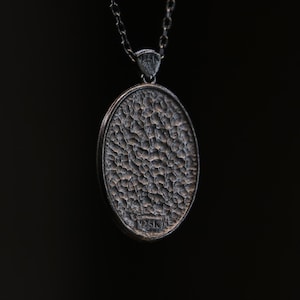 May include: A silver pendant necklace with a round, textured silver charm. The charm has a 925K stamp on the back.