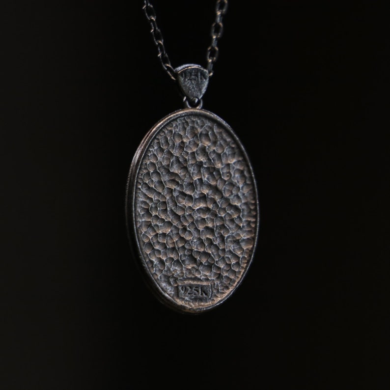 May include: A silver pendant necklace with a round, textured silver charm. The charm has a 925K stamp on the back.