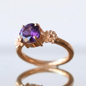 Puede incluir: Una taza de cerámica blanca con un asa negra y el texto "But First, Coffee" en negro, con una fuente de estilo manuscrito. La taza está sobre una superficie blanca.