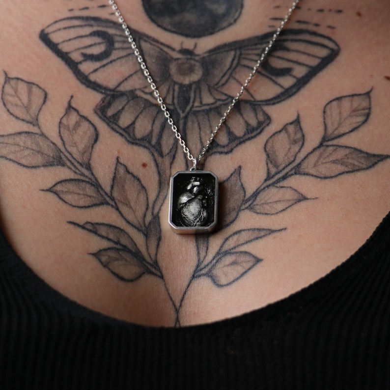 May include: A silver chain necklace with a square pendant featuring a black and white anatomical heart image.