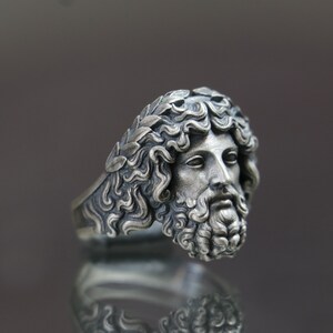 May include: A silver ring with a detailed sculpted face of a man with a beard and a laurel wreath on his head.