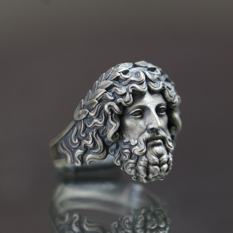 May include: A silver ring with a detailed sculpted face of a man with a beard and a laurel wreath on his head.
