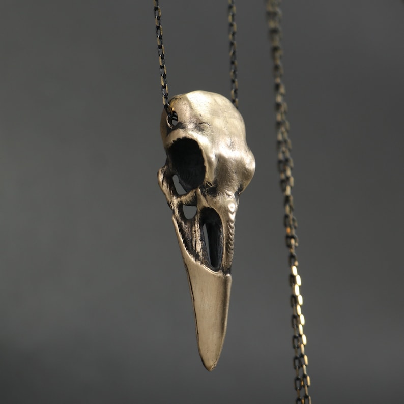 May include: A gold-toned pendant necklace featuring a detailed bird skull design. The pendant is attached to a delicate chain.