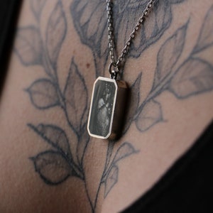 May include: A silver chain necklace with a rectangular pendant featuring a black and white image of a heart.