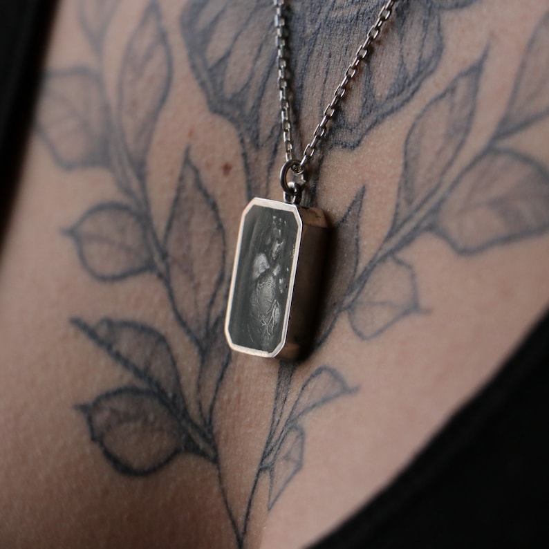 May include: A silver chain necklace with a rectangular pendant featuring a black and white image of a heart.