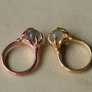 May include: Two rings with a clear crystal orb held by two hands. One ring is rose gold and the other is gold.