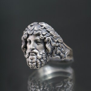 May include: A silver ring with a detailed sculpted head of a man wearing a laurel wreath. The ring is a statement piece with a classic design.