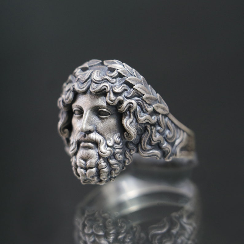 May include: A silver ring with a detailed sculpted head of a man wearing a laurel wreath. The ring is a statement piece with a classic design.