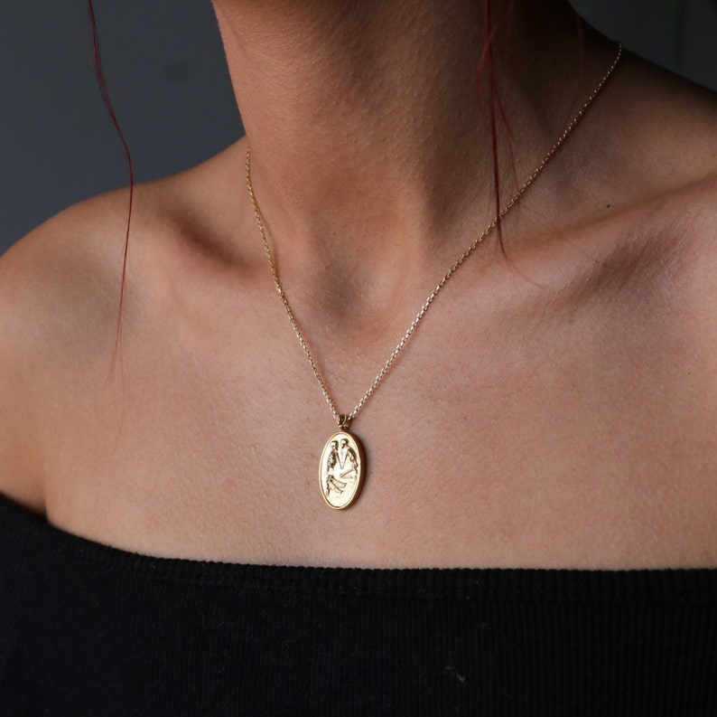 May include: A gold chain necklace with a gold oval pendant featuring a detailed design of two birds.