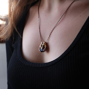 May include: A gold necklace with a pendant shaped like a hand holding a dark purple gemstone.