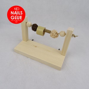 May include: Wooden toy for small animals, featuring a rotating wooden dowel with a series of colourful balls attached. The toy is mounted on a wooden stand. The stand has a sign that reads "NO NAILS or GLUE USED ON THIS PRODUCT".