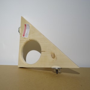 May include: A triangular wooden object with a large circular cutout. The wood is light-coloured with visible grain. Metal hardware is attached at two points. A red and white clearance sticker is affixed to the wood.