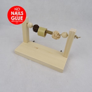 May include: Wooden toy for small animals, featuring a rotating wooden dowel with a series of colourful balls attached. The toy is mounted on a wooden stand. The stand has a sign that reads "NO NAILS or GLUE USED ON THIS PRODUCT".