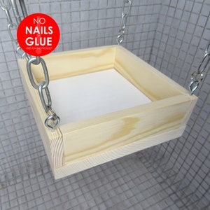 May include: A wooden hanging shelf with a white surface. The shelf is suspended by two silver chains. The shelf is labelled "NO NAILS or GLUE USED ON THIS PRODUCT".