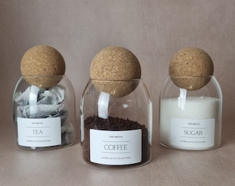 May include: Three glass jars with cork lids, each containing a different kitchen staple: tea bags, coffee grounds, and white sugar. The jars are labelled "The Smiths" and have the product name printed below. The labels also include the text "Laybella Co Collection."
