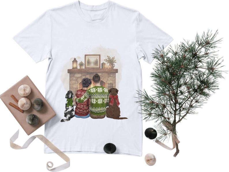 May include: A white t-shirt featuring a graphic illustration of two people sitting in front of a stone fireplace. The people wear patterned sweaters, and two dogs sit beside them. The fireplace mantel holds a framed picture, a lantern, and plants.
