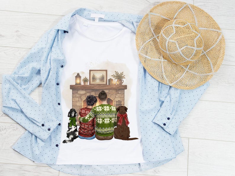 May include: A white t-shirt featuring a graphic illustration of two people and two dogs sitting before a stone fireplace. The people wear patterned sweaters, and the dogs wear festive scarves. A light blue button-down shirt and a straw hat are included.
