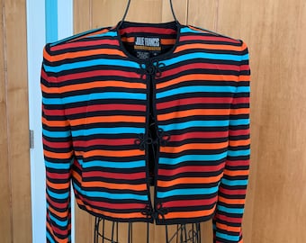 May include: A striped cropped jacket with long sleeves and a mandarin collar. The jacket is black with orange, red, and blue stripes. The jacket has black buttons with a knotted design.