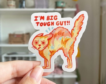 May include: A sticker featuring a cartoon cat with a yellow and orange patterned fur. The cat is arched with its back legs straight and its front legs bent. The cat has a surprised expression on its face. The sticker has the text "I'm Big Tough Guy!" in red letters.