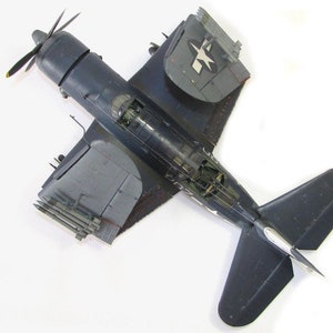May include: A dark blue model airplane with a white star on the wing. The plane has a propeller and is sitting on a white surface.