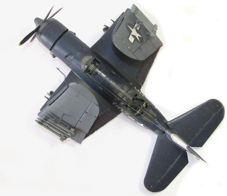 May include: A dark blue model airplane with a white star on the wing. The plane has a propeller and is sitting on a white surface.