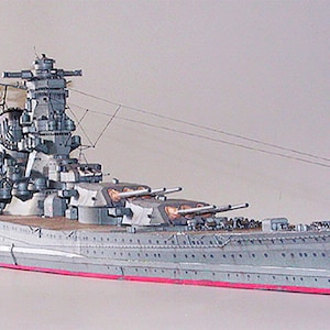 May include: A detailed model of a Japanese battleship, painted in a grey colour scheme with red accents. The model features intricate details, including multiple gun turrets, a complex superstructure, and a long, slender hull.