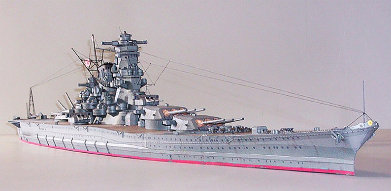 May include: A detailed model of a Japanese battleship, painted in a grey colour scheme with red accents. The model features intricate details, including multiple gun turrets, a complex superstructure, and a long, slender hull.
