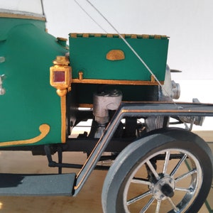 Puede incluir: Un coche modelo verde y dorado con un guardabarros negro y una rueda cromada. El coche tiene una peque&ntilde;a luz roja en el lateral y un ribete dorado alrededor de la carrocer&iacute;a.