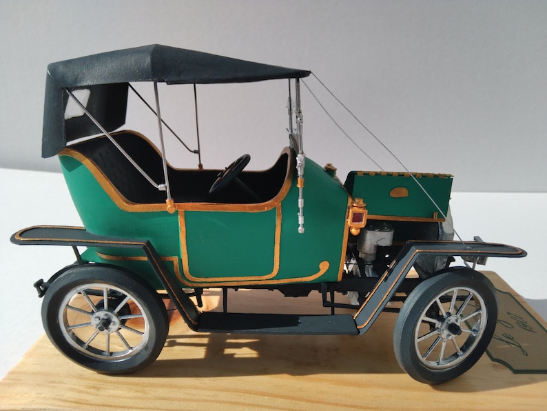 Puede incluir: Un coche modelo verde y dorado con capota de lona negra. El coche tiene un motor y ruedas detallados.