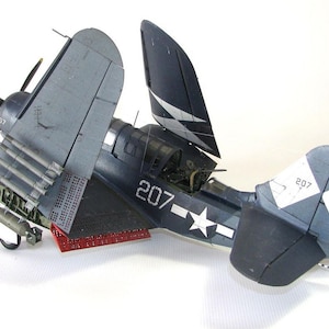 May include: A blue and white model airplane with the number 207 on the side. The plane has its wings folded back and is sitting on a white surface.