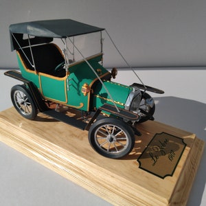 Puede incluir: Un coche modelo verde y negro con capota de tela negra. El coche est&aacute; sobre una base de madera con una placa dorada que dice "Le Debene 1907".