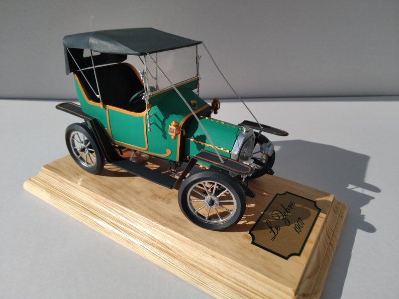 Puede incluir: Un coche modelo verde y negro con capota de tela negra. El coche est&aacute; sobre una base de madera con una placa dorada que dice "Le Debene 1907".