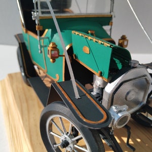 Puede incluir: Primer plano de un coche modelo verde y negro con un motor plateado. El coche tiene un ribete dorado y un parabrisas. El coche est&aacute; sobre una base de madera.