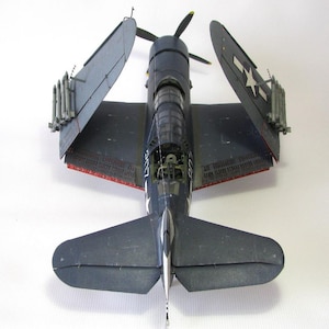 May include: A blue and gray model airplane with its wings folded up. The model has a white star on the side and is sitting on a white surface.