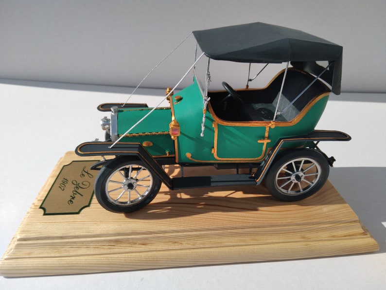 Puede incluir: Un coche modelo verde y negro con una capota de tela negra. El coche est&aacute; sobre una base de madera con una placa dorada que dice "Le De Dion 1902".