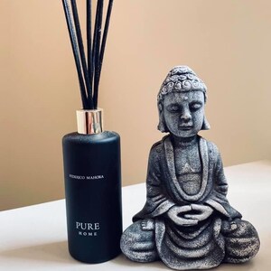 K&ouml;nnte beinhalten: Eine schwarze Diffuserflasche mit schwarzen Ruten und dem Text "Federico Mahora Pure Home" auf dem Etikett. Eine graue Steinbuddha-Statue sitzt vor dem Diffusor.
