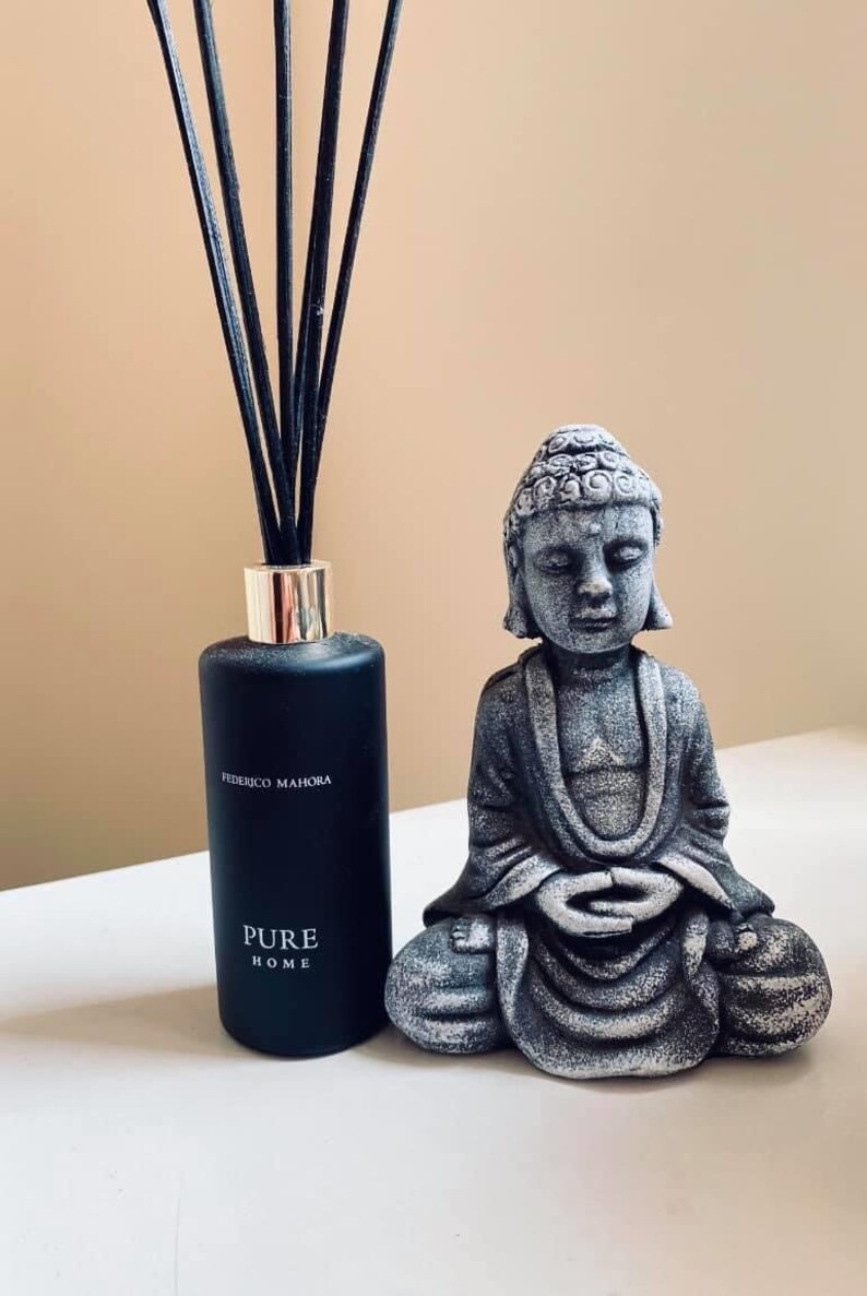 K&ouml;nnte beinhalten: Eine schwarze Diffuserflasche mit schwarzen Ruten und dem Text "Federico Mahora Pure Home" auf dem Etikett. Eine graue Steinbuddha-Statue sitzt vor dem Diffusor.
