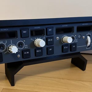 Peut inclure: Un tableau de bord d'avion gris foncé avec divers boutons, molettes et écrans. Le panneau est monté sur un support noir. Le panneau présente des accents blancs et orange. Le panneau comprend le texte "CONTROL", "A/T ARM", "IAS MACH", "ALTITUDE" et "SPEED".