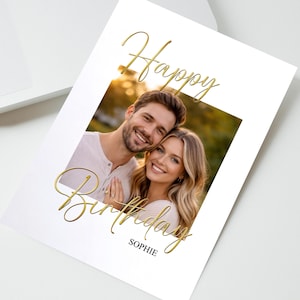 May include: A rectangular white greeting card featuring a central photograph of a smiling couple. The card displays the gold cursive text Happy Birthday above and below the photo, with the name SOPHIE printed in black capital letters at the bottom.