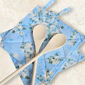 May include: Two wooden spoons on top of a set of blue quilted pot holders with a white floral pattern.